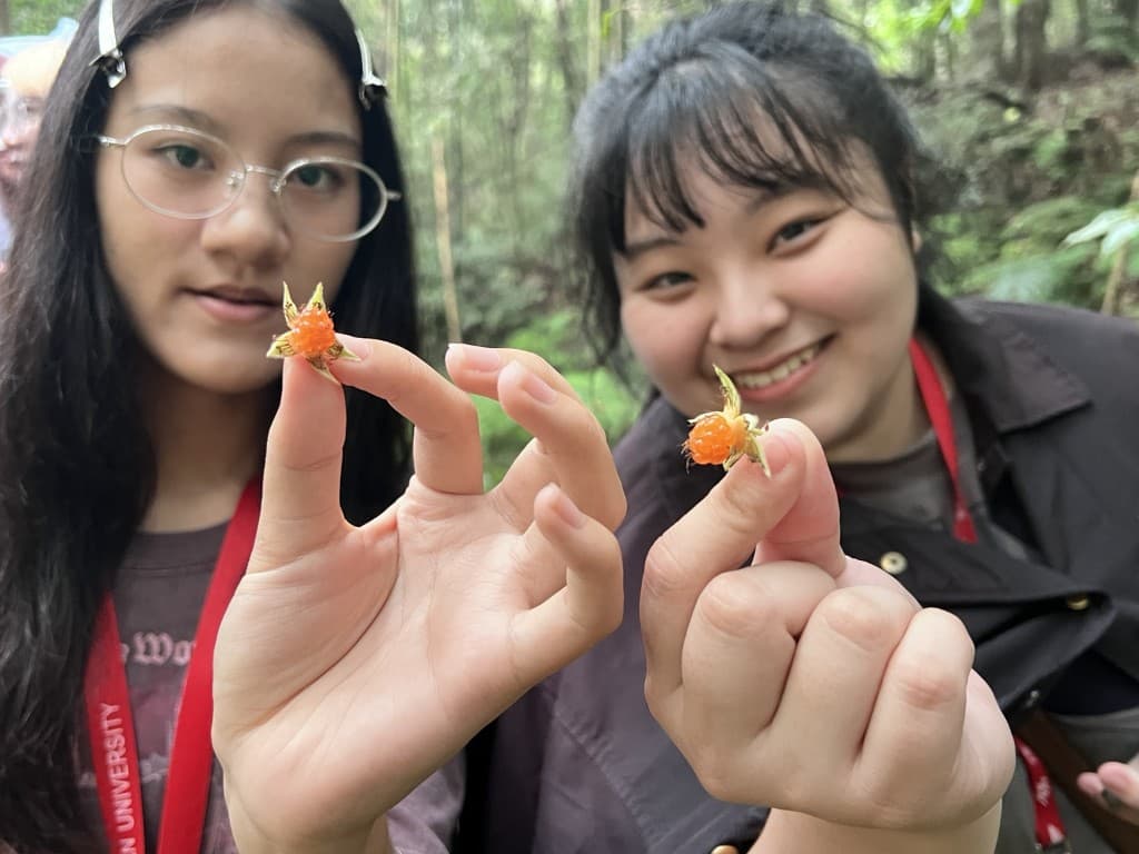 Two students holding small orange wild fruits found in the forest