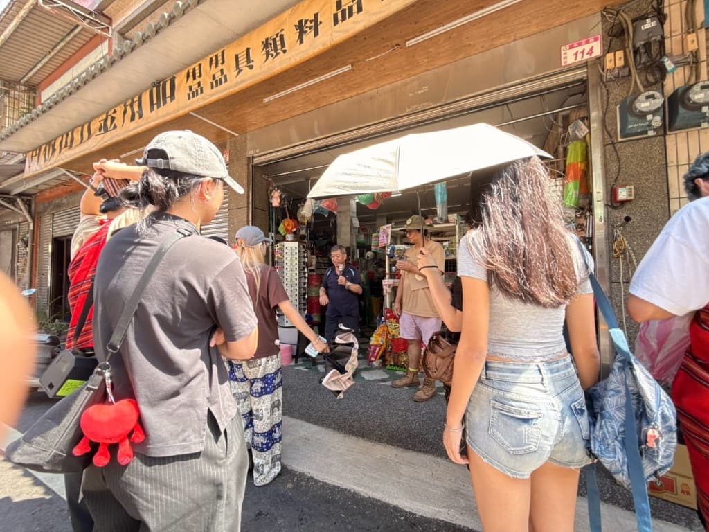 Students standing outside Ri Wang Hardware Store while owner Mr. Yu shares memories of the shop and the street
