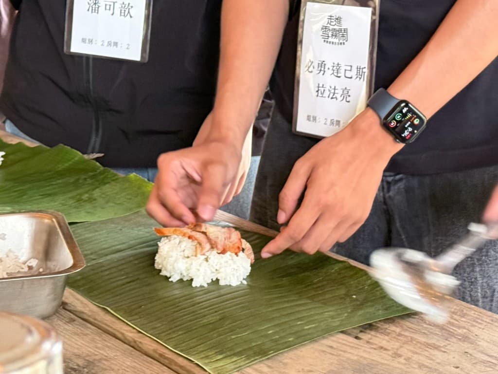 Hands placing grilled meat on rice set over a banana leaf