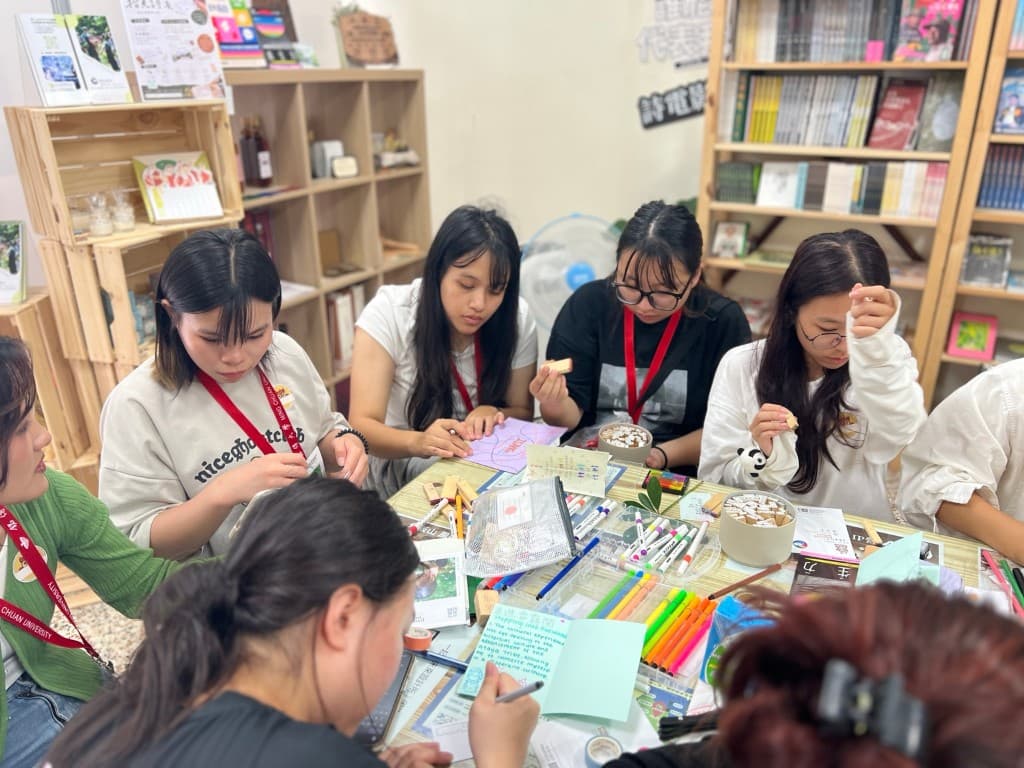 Students gathered around a bookshop table, drawing and working with materials